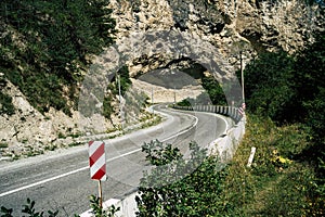 Curvy road with traffic signs in mountains. Red diagonal keep left obstacle traffic sign placed on stone border of curvy