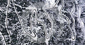 Curvy Windy Mountain Road in Snow Covered Forest. Aerial top down in Winter