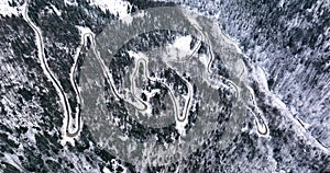 Curvy Windy Mountain Road in Snow Covered Forest. Aerial top down in Winter