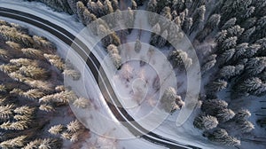 Curvy windy road in snow covered forest top down aerial view