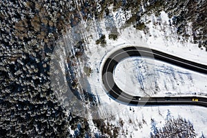 Curvy windy road in snow covered forest, top down aerial view. Winter landscape