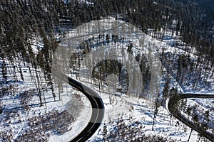 Curvy windy road in snow covered forest, top down aerial view. Winter landscape