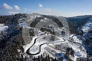 Curvy windy road in snow covered forest, top down aerial view. Winter landscape