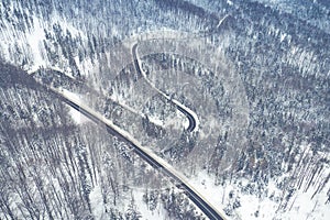 Curvy windy road in snow covered forest, top down aerial view. Winter landscape