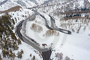 Curvy windy road in snow covered mountain hill. Top down aerial view. Scenic winter background captured from above