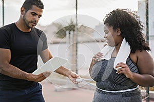 Curvy woman with her personal trainer measuring body waist outdoor - Focus on african girl face