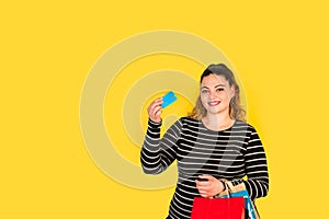 Curvy woman smiling with a credit card in her hand and shopping bags in the other