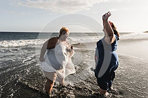 Curvy women dancing on the beach having fun during summer vacation - Focus on left woman