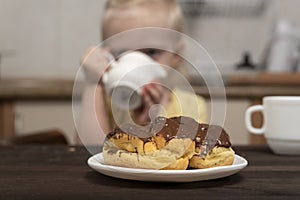 Custard cakes on the table. Little girl on background drinks a milk. Breakfast with child