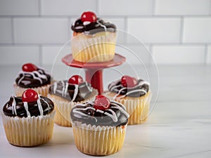 Custard filled yellow cupcake with chocolate frosting and white swirls with a red cherry on top!  Delicious baked goods on a