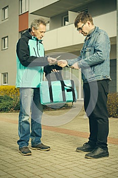 Customer assuming a pizza food from a delivery man on sidewalk