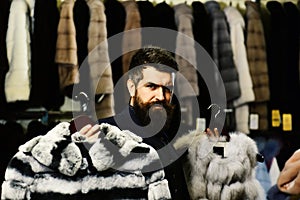 Customer with beard presents furry coats. Businessman with expensive overcoats