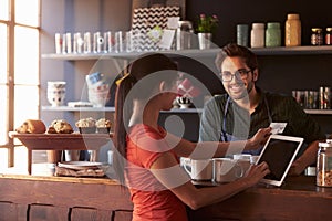 Customer In Coffee Shop Paying Using Digital Tablet Reader