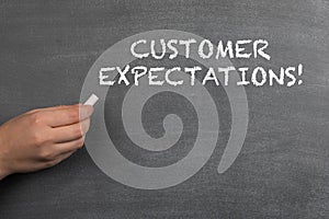 CUSTOMER EXPECTATIONS. White chalk in a woman`s hand. Black chalk board