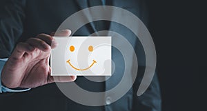 Customer Experience Concept, Businessman holding Card with Smiley Happy Face for his Satisfaction. feedback rating and positive cu