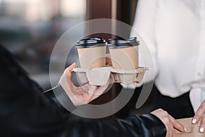 Customer in face mask stand outdoors and take package with coffee from cashier in mask at cafe. Take away food. Close up