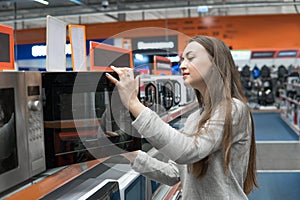 Customer girl chooses a microwave oven in a home appliance store