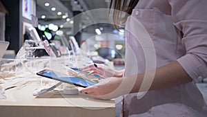 Customer girl in electronics store uses modern tablet computer near presentation showcase