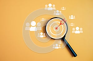 Customer group icons in a magnifying glass placed on a yellow background represent the selection of business goals, target