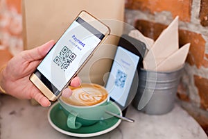 Customer hand using smart phone to scan QR code tag on another smart with coffee in coffee shop or restaurant