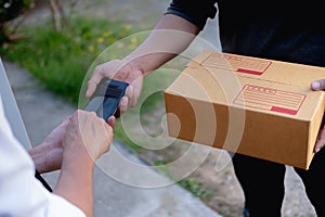 Customer hands appending signature in mobile phone, man receiving parcel post box from courier with delivery service man, express