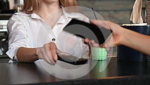 The customer makes a payment via mobile phone to buy a drink. A female seller holds an electronic reader, and a female