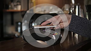 Customer paying with NFC technology by mobile phone on terminal in modern cafe