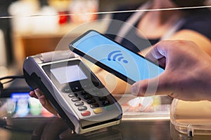 Customer is paying with smartphone in shop using NFC technology. against the background of the payment terminal and the seller`s