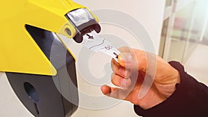 Customer pulls with hand a numbered ticket out of yellow number dispenser machine, to wait in service line and to be served when h