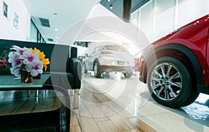 Customer reception area and blur red and white luxury SUV car parked in modern showroom. Car dealership and auto leasing concept.