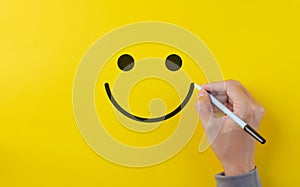 Customer review satisfaction feedback survey concept. Hand using pen to draw happy smiling face on yellow background. Service