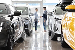 Customer and sales assistant shaking hands, car showroom interior