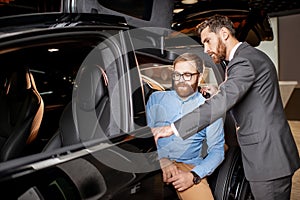 Customer with a sales manager inspecting modern car in the showroom