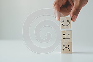 Customer satisfaction concept. Hand lifts smiling face and sad face icon on wood cube block.
