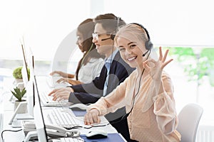 Customer service executive showing okay gesture and her colleagues working at call centre
