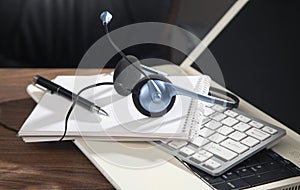 Customer service headset, computer keyboard and business objects on the wooden table