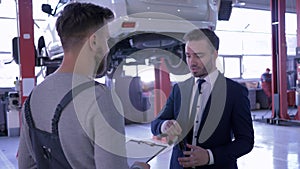 Customer shakes hands with auto repair service represantative and gives car keys on background of the vehicle on a