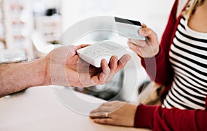 Customer and shop assistant making contactless payment using credit card in a shop.