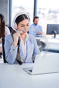 Customer support agent woman in headset with microphone talking to client and using laptop at call center.