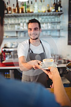 Customer taking coffee from happy waiter at cafe