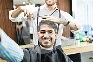 Customer Taking Selfie While Stylist Cutting His Hair With Scissors