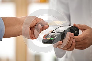 Customer using terminal for contactless payment with credit card in pharmacy
