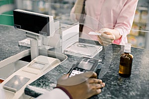 Customer woman making payment in drugstore. Pharmacist holding terminal, woman paying for drugs with credit card. Modern