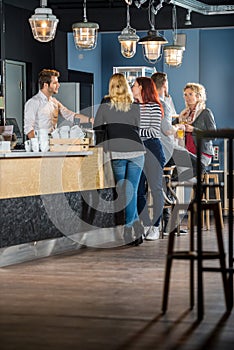Customers With Bartender Standing At Counter