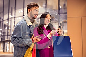 customers couple with many shopping bags look at smartphone outside
