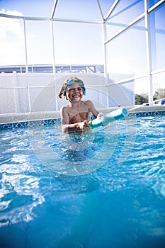 Cut African American little boy shooting a water gun while playing with friends in a backyard swimming pool.