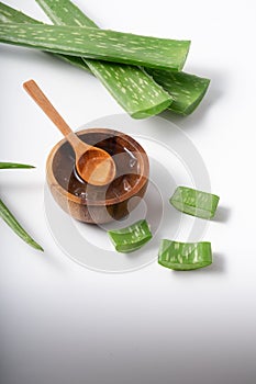 Cut aloe vera stem and gel in wooden bowl on white background