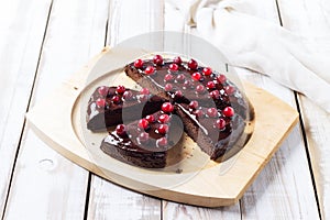 Cut into chunks of gluten-free Brownie cake with chocolate icing, decorated with cranberries, on a light wooden table.