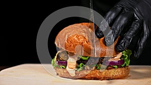 Cut craft burger is cooking on black background. Consist sauce salsa, lettuce, red onion, pickle, cheese, chilli green