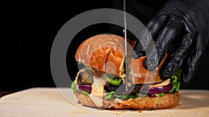 Cut craft burger is cooking on black background. Consist sauce salsa, lettuce, red onion, pickle, cheese, chilli green